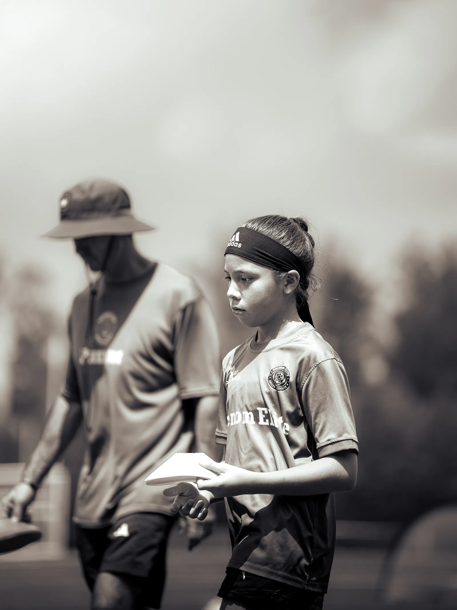 A Phenom Elite player holding training markers beside a coach on the field